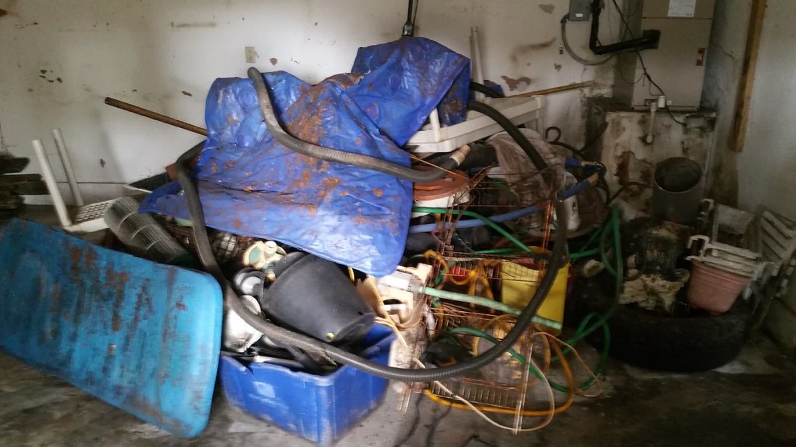 A garage corner buried under tarps, hoses, bins, and hardware